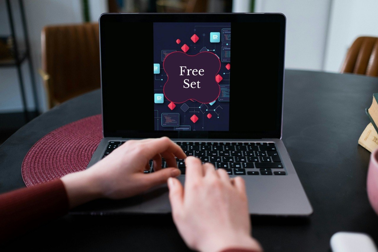 A person's hands typing on a laptop computer on a dark table. The laptop screen displays a digital graphic with the text 'Free Set' inside a purple frame, surrounded by abstract red and blue geometric shapes.