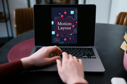A person typing on a laptop at a dark table, with the laptop screen displaying a presentation template titled 'Motion Layout'.
